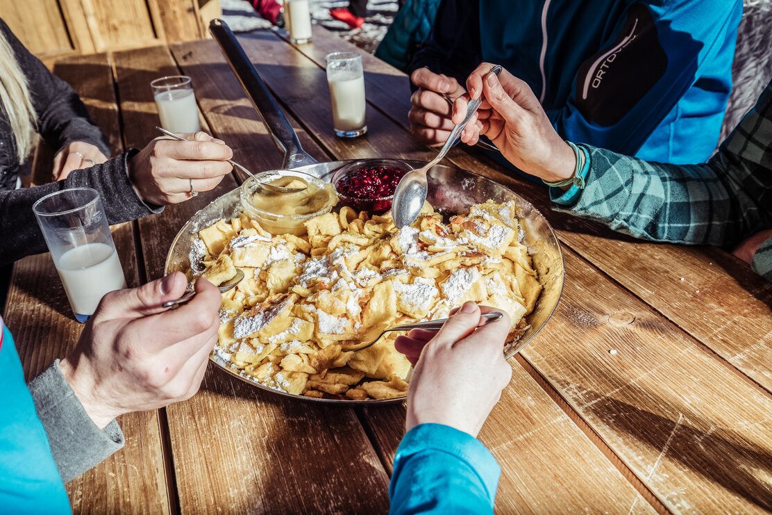 Auf diesem Bild zu sehen ist eine Pfanne voller Kaiserschmarrn mit einer kleinen Schüssel Apfelmus und einer kleinen Schüssel Preiselbeeren