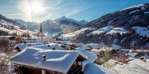 Winterurlaub im Alpbachtal Alle Häuser voller Schnee, die Sonne scheint durch das Dorfzentrum von Alpbach, im Hintergrund die pure Winterlandschaft