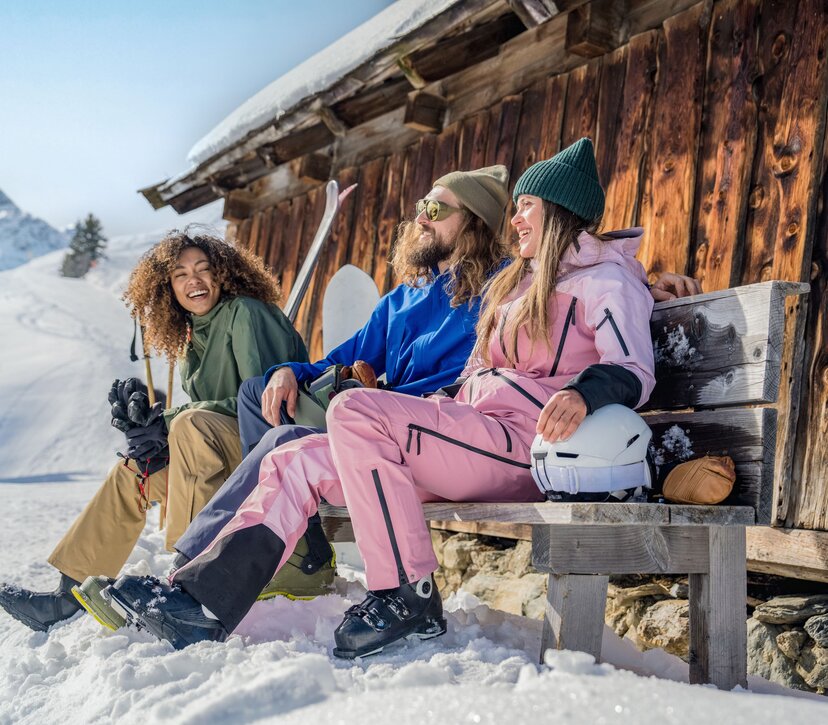 Zwei Frauen und ein Mann sitzen auf einer Bank neben einer Hütte - ihre Ski lehnen an der Hütte. | © Ski Juwel Alpbachtal Wildschönau | Christoph Oberschneider