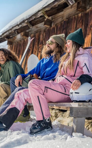 Zwei Frauen und ein Mann sitzen auf einer Bank neben einer Hütte - ihre Ski lehnen an der Hütte. | © Ski Juwel Alpbachtal Wildschönau | Christoph Oberschneider